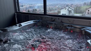 A hot tub with a view of a town and mountains through large windows. - Rooms & Spa BJELASICA (Bijelo Polje)