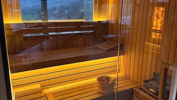 A sauna with wooden benches and a glass enclosure, a wooden bench with a bucket, and a small shelf with items.