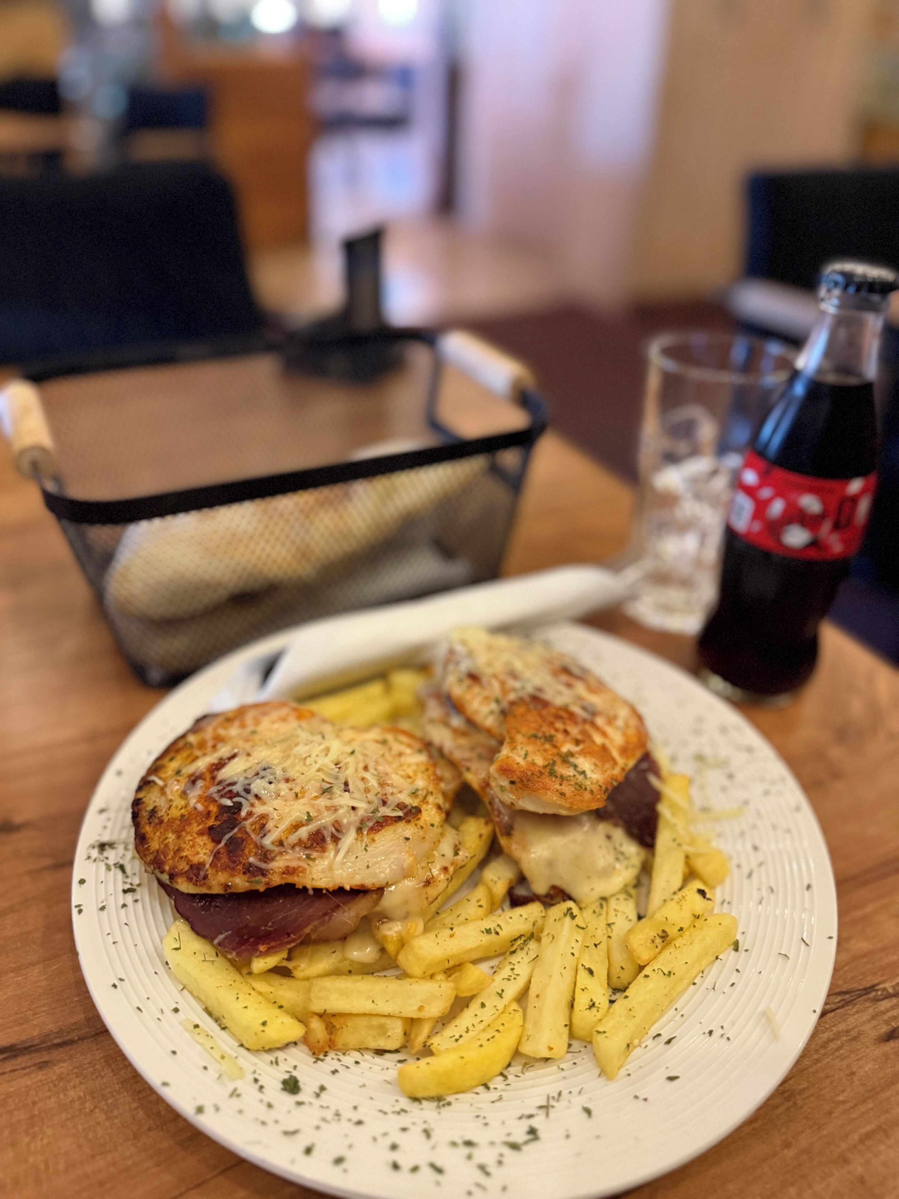 Un plato de comida con papas fritas y un sándwich, un vaso de refresco y una botella sobre una mesa.