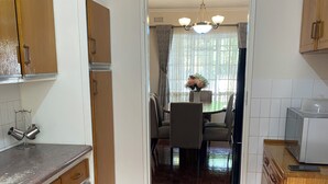 Een keuken met houten kasten, een betegelde vloer en een eethoek met een tafel en stoelen.