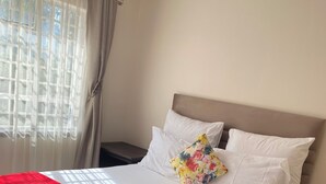 Een hotelkamer met een bed, nachtkastje, rode plaid en een raam met gordijnen.