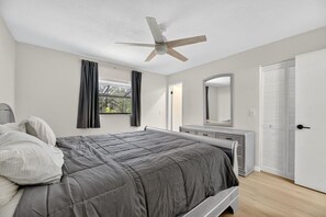 A bedroom with a bed, a ceiling fan, a window with curtains, a dresser, a mirror, and a closet. - Beautiful 2/2 Pool Home in Spring Hill (Spring Hill)