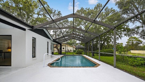 A covered swimming pool with a white exterior, a metal roof, and a view of a house in the background. - Beautiful 2/2 Pool Home in Spring Hill (Spring Hill)