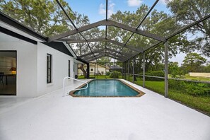 A covered swimming pool with a white exterior, a metal roof, and a view of a house in the background. - Beautiful 2/2 Pool Home in Spring Hill (Spring Hill)