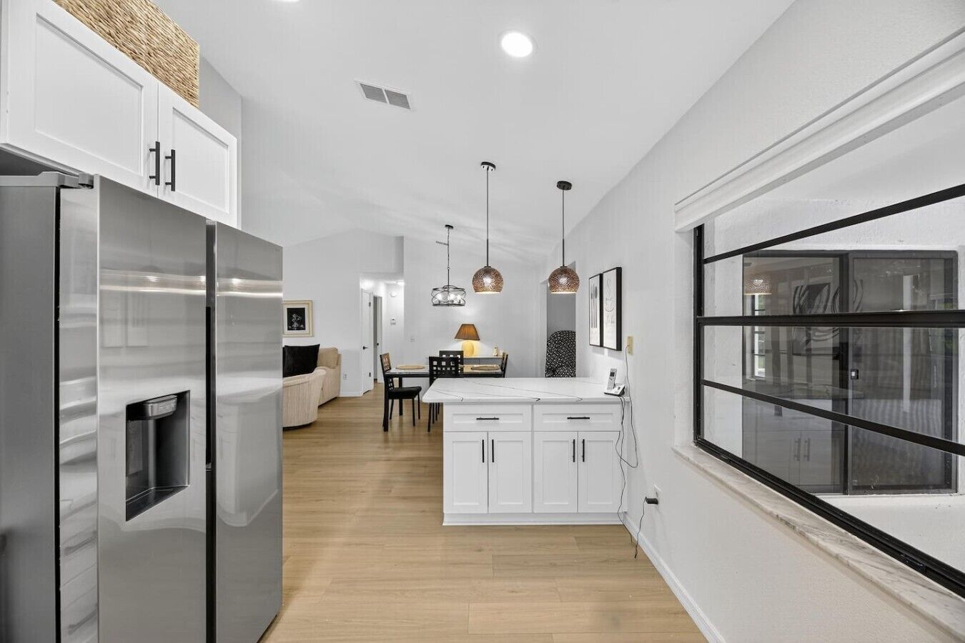 A modern kitchen with white cabinetry, a built-in refrigerator, pendant lighting, and a large window.