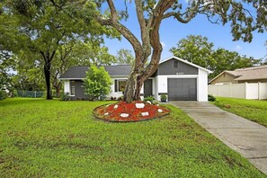 A residential house with a garage, a well-maintained lawn, and a tree in the front yard. - Beautiful 2/2 Pool Home in Spring Hill (Spring Hill)