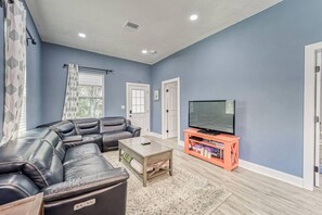 A living room with a sectional sofa, a coffee table, a TV on a stand, and a door. - Modern West Tampa Bungalow - Live & Work In Style (Tampa)