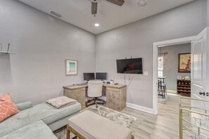 A living room with a sofa, a desk with two monitors, a TV, and a dining area with a wine rack. - Modern West Tampa Bungalow - Live & Work In Style (Tampa)