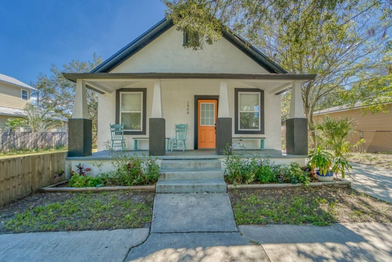 A single-story house with a front porch, a door, and a small garden area.