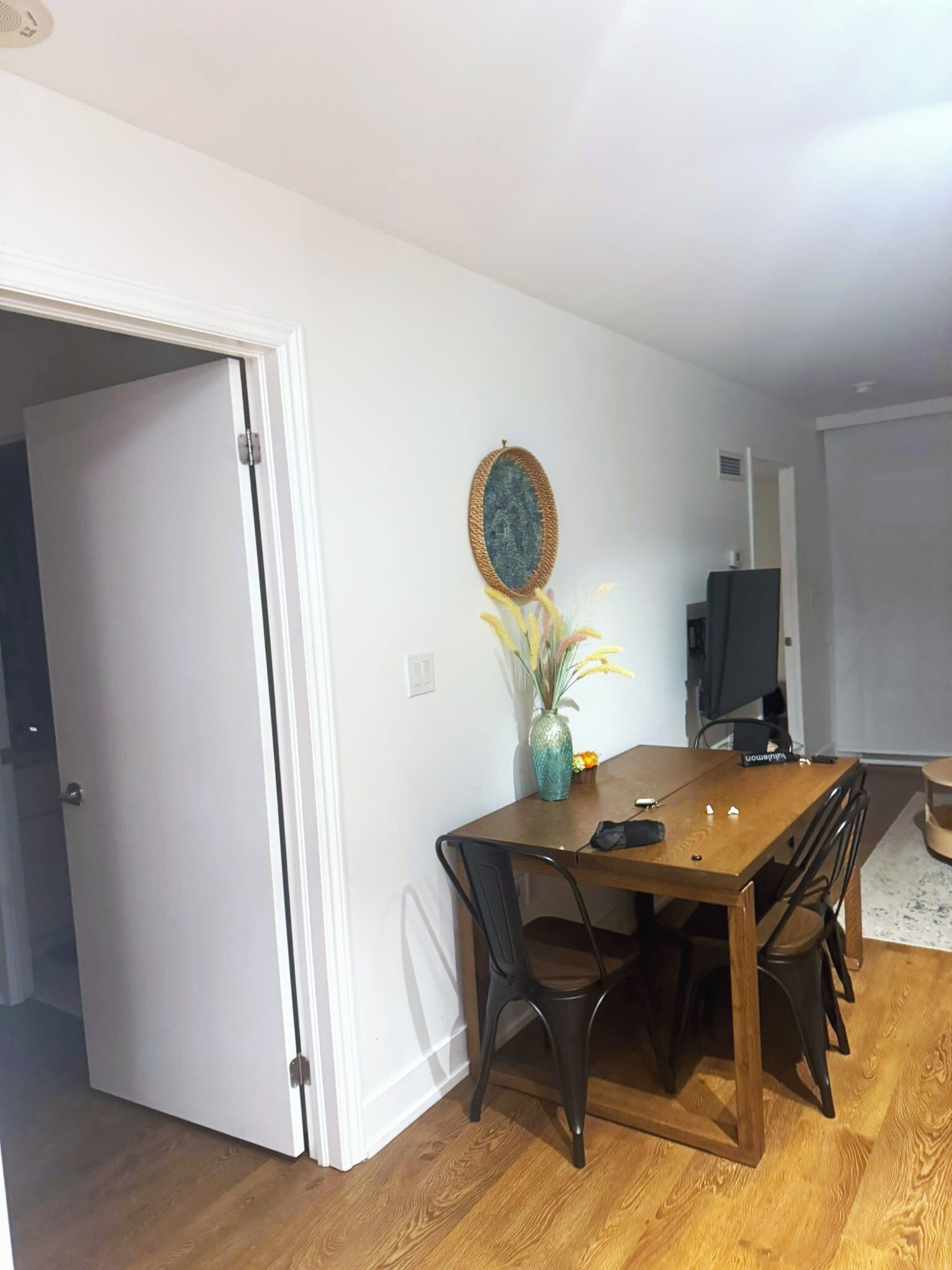 A dining area with a wooden table, four chairs, a vase with flowers, and a television in the background.