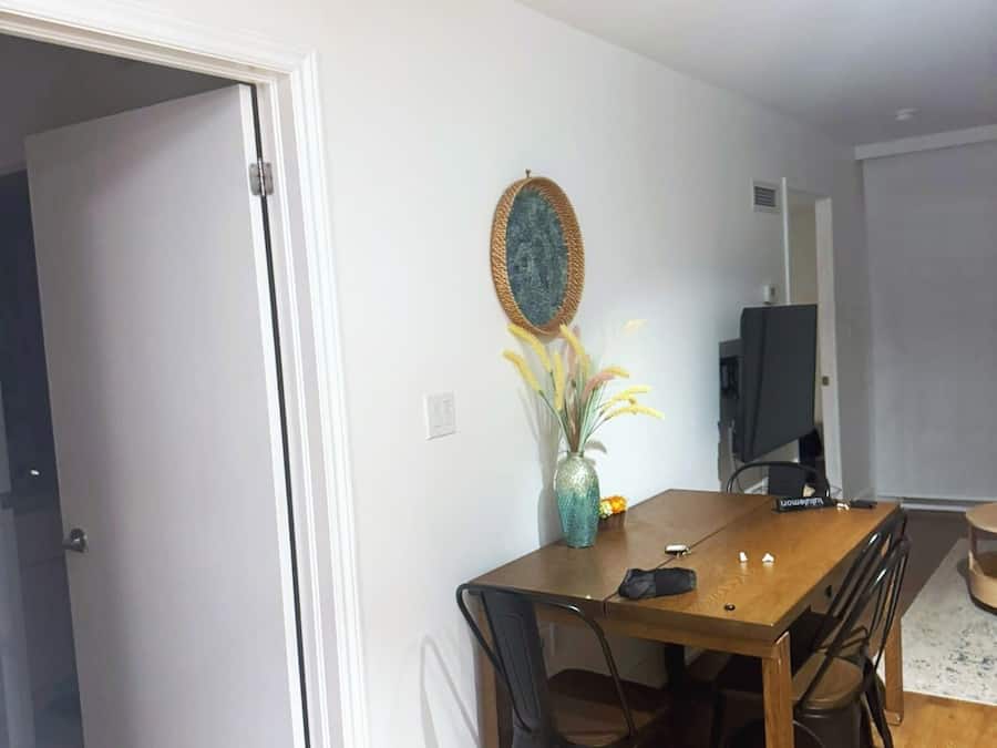 Un comedor con una mesa de madera, cuatro sillas, un jarrón con flores y un televisor al fondo.