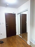 Una habitación con piso de madera, una puerta de madera oscura, una puerta corredera de vidrio y una pared blanca con un interruptor de luz.