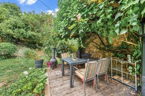 Eine sonnige Terrasse mit Tisch und Stühlen, umgeben von üppigem Grün und einer Steinmauer.