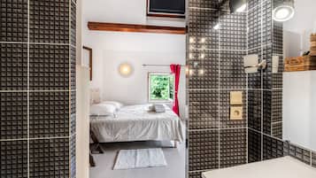 Un dormitorio moderno con cama, mesita de noche, ventana con vistas a zonas verdes, y baño con espejo y lavamanos.