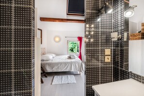 Ein modernes Schlafzimmer mit Bett, Nachttisch, Fenster mit Blick auf Grünflächen und einem Badezimmer mit Spiegel und Waschbecken.