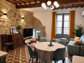 Ein gemütliches Wohnzimmer mit Steinwand, Fernseher, Esstisch und einer Couch.
