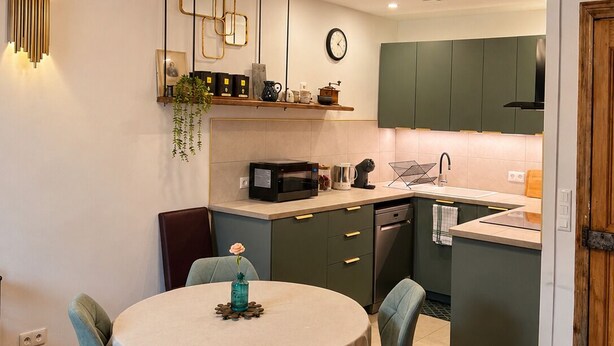 Une cuisine moderne avec des meubles de rangement verts, une table de salle à manger ronde entourée de chaises et un sol à motifs géométriques.