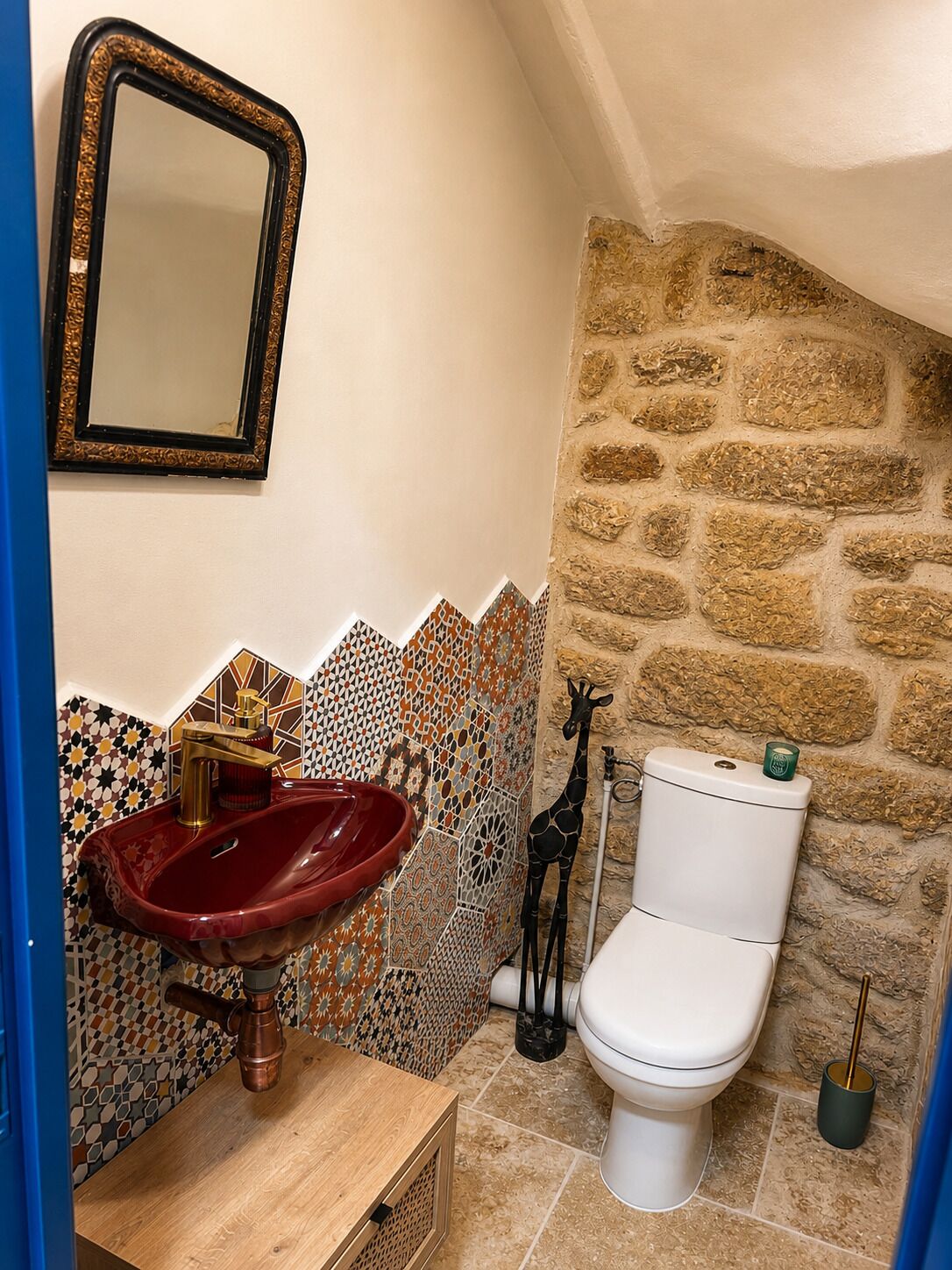 Une salle de bain avec un lavabo rouge, des toilettes blanches et un mur en pierre.