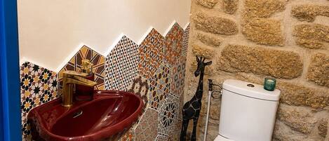 Un baño con un lavabo rojo, inodoro blanco y pared de piedra.