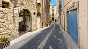 Une rue étroite bordée d’immeubles en pierre, avec une porte bleue et une enseigne indiquant un magasin de tissus.