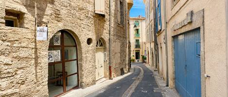 Una calle estrecha con edificios de piedra, una puerta azul y un letrero de una tienda de telas.