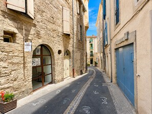 Eine enge Straße mit Steinhäusern, einer blauen Tür und einem Schild für ein Stoffgeschäft.