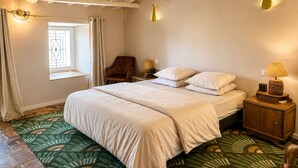 Une chambre à coucher comprenant un lit, une chaise, une table de chevet, une lampe, une fenêtre avec des rideaux et un tapis à motifs.