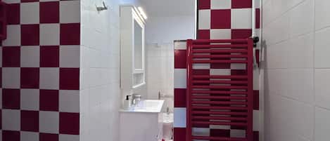 A bathroom with a checkered floor pattern, a white sink, a mirror, and a red towel rack.