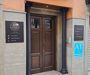 A hotel entrance with a double door, a signboard with hotel name and contact information, and a blue sign indicating AT services. - La Perla Reyes Católicos Living: Standard Apartment (Granada)