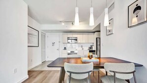 A modern kitchen with white cabinets, a dark countertop, and a dining area with two chairs and a table. - Ocean and Canal View Condo Beach 8 min Pool 1906 (Hallandale Beach)