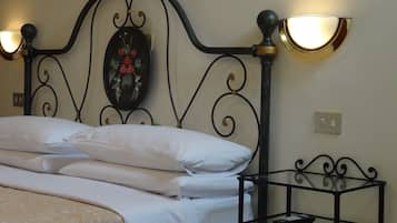 A neatly made bed with white linens and a floral-patterned duvet, a wall-mounted decorative mirror, and a small bedside table with a remote control.
