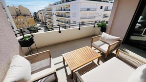A balcony with wicker furniture, a wooden table, and a view of adjacent buildings. - JUST 250 METRES FROM THE FAMOUS BOULEVARD DE LA CROISETTE AND ITS SANDY BEACHES (Cannes)