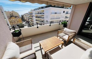 A balcony with wicker furniture, a wooden table, and a view of adjacent buildings. - JUST 250 METRES FROM THE FAMOUS BOULEVARD DE LA CROISETTE AND ITS SANDY BEACHES (Cannes)