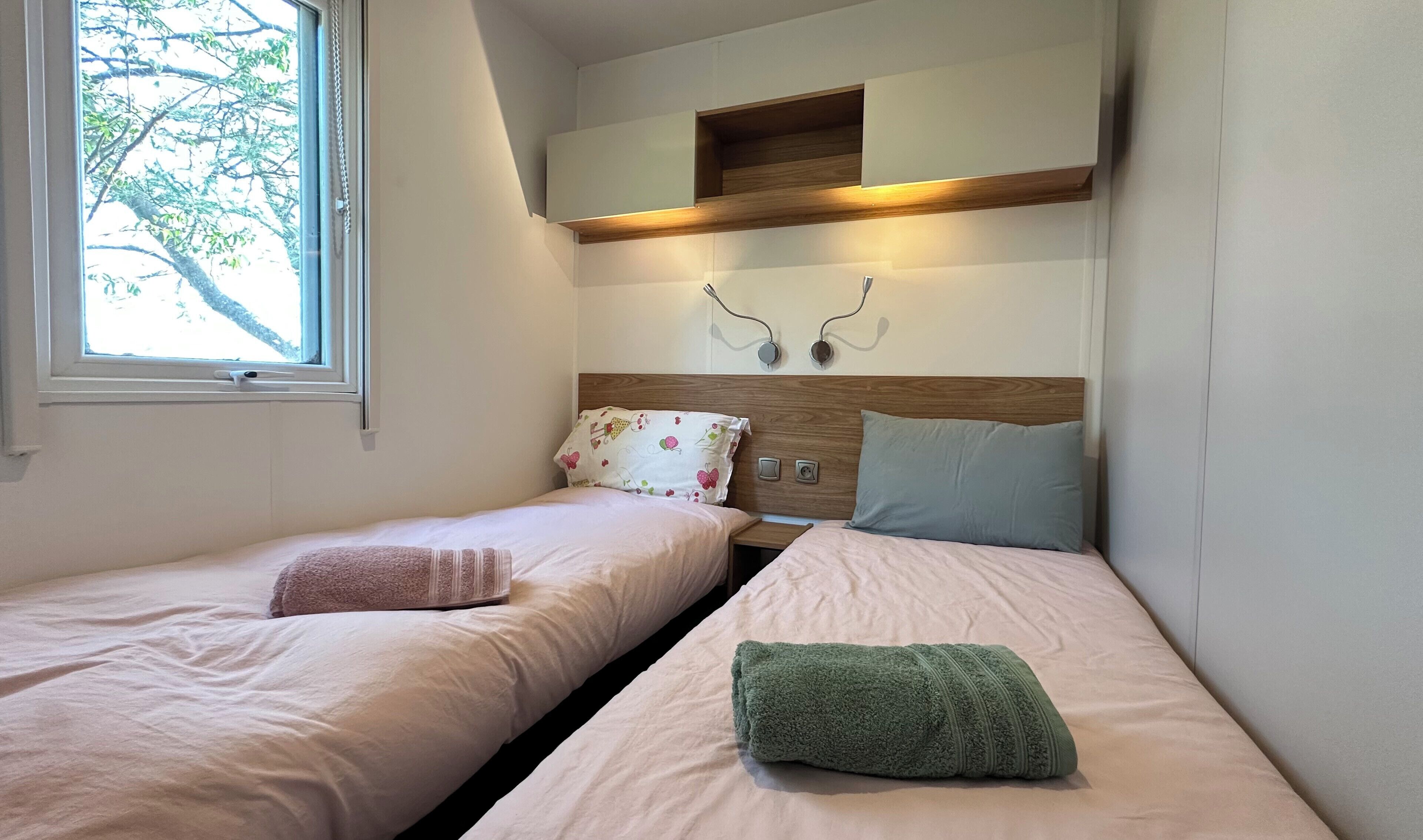 Een slaapkamer met twee bedden, een raam en een wandplank.