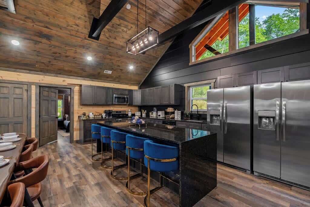 A modern kitchen with a large island, stainless steel appliances, and a bar area with blue bar stools.