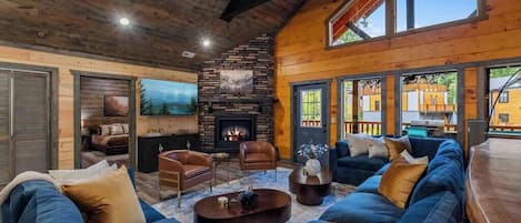 A cozy living room with a stone fireplace, leather sofas, and a large window overlooking the outdoors.