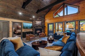 A cozy living room with a stone fireplace, leather sofas, and a large window overlooking the outdoors. - 8-Bedroom Cabin with Themed Indoor Pool, Theater & Arcade Near Pigeon Forge (Sevierville)