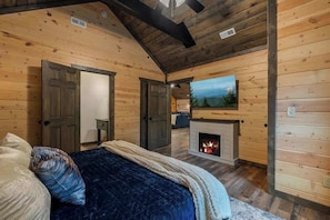 Ein Schlafzimmer in einer Blockhütte mit Kamin, einem Bett mit blauer Decke und einem Bild an der Wand.