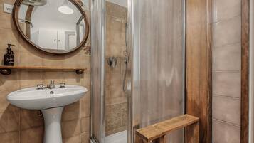 Une salle de bain avec un lavabo sur colonne, un espace douche, une étagère en bois et un miroir.