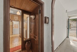 A wooden door leading to a room with a radiator, a large vase, and a framed picture on the wall.
