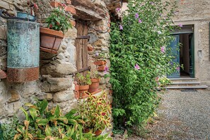Un mur de pierres rustiques agrémenté de plusieurs pots de fleurs et d’une plante grimpante aux fleurs violettes.