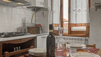 A kitchen with white tiles, a gas stove, a bottle, a glass carafe, and a dining table set with plates and cutlery.