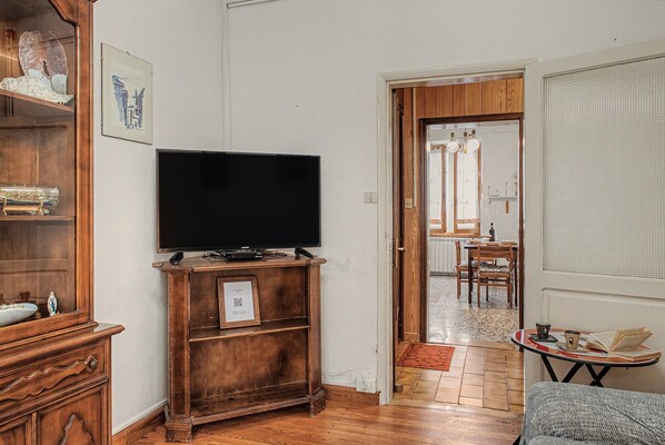 A living room with a television on a wooden stand, a dining area with a table and chairs, and a kitchen visible through an open door.