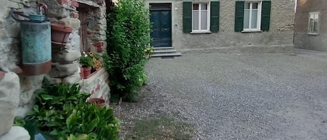 A stone building with a gravel courtyard, a green door, and shutters.