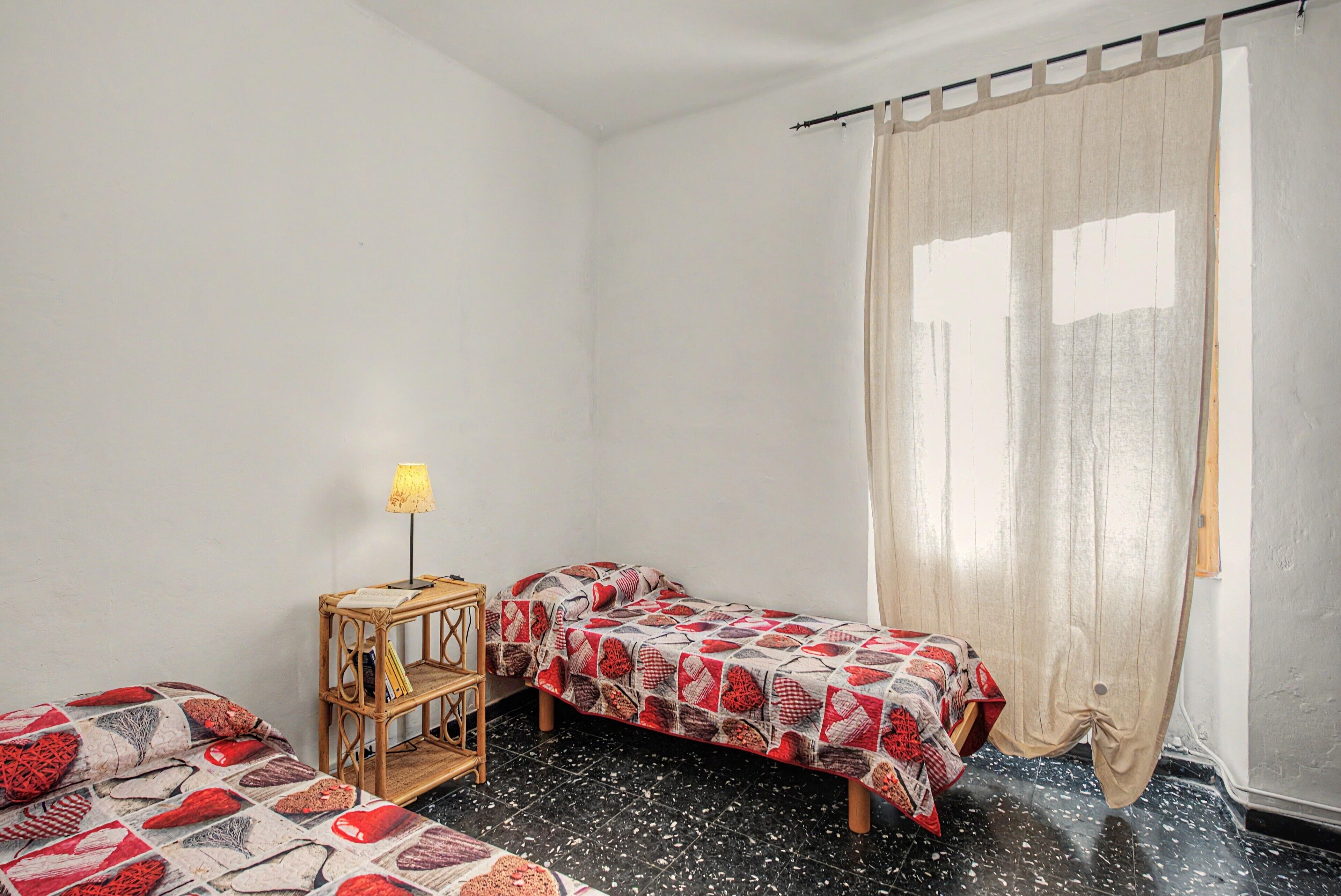 A small, clean room with two beds, a bedside table with a lamp, and a window with a curtain.