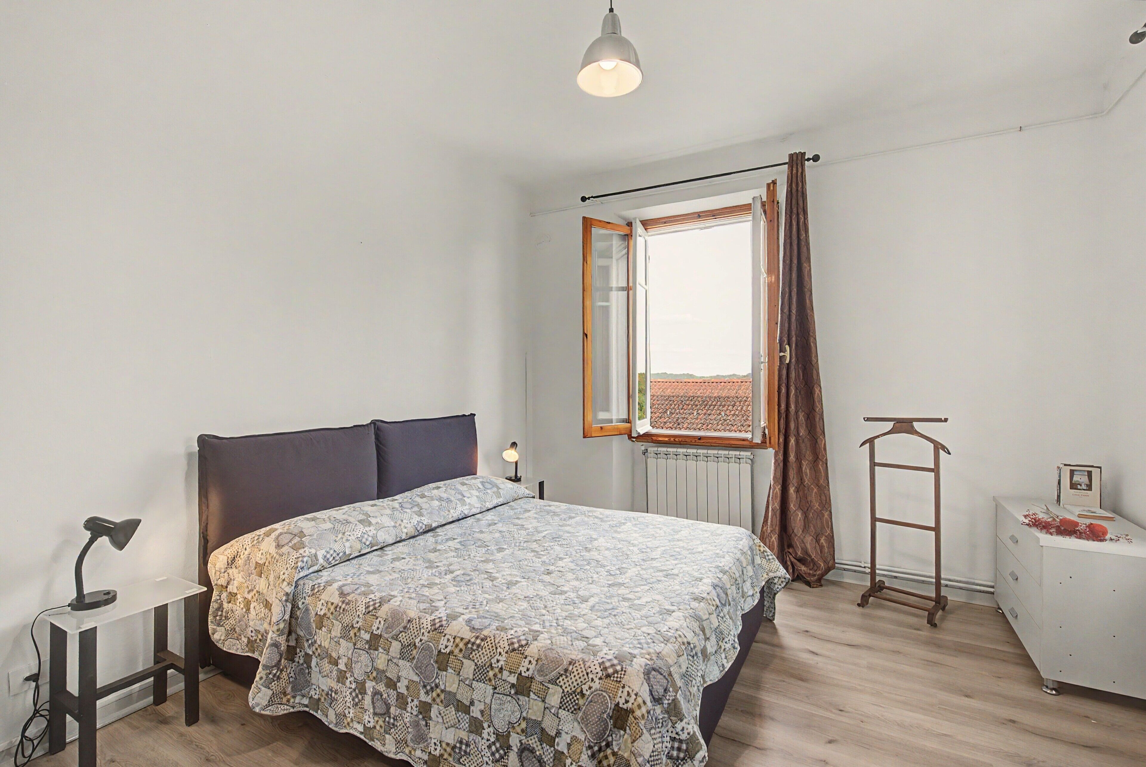 A bedroom with a bed, a bedside lamp, a radiator, a window with curtains, and a wooden ladder.