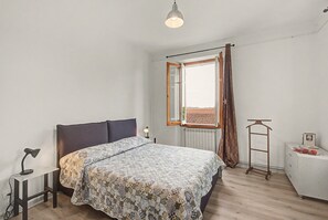 A bedroom with a bed, a bedside lamp, a radiator, a window with curtains, and a wooden ladder.