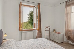 A bedroom with a bed, a dresser, a radiator, and a window with curtains.