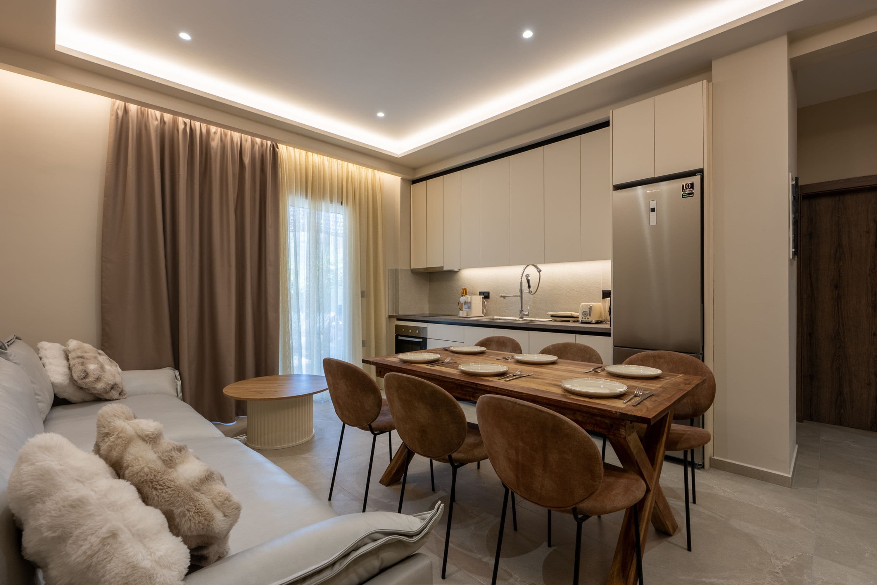 Una sala moderna con un sofá, una mesa de comedor para cuatro comensales y una cocina con electrodomésticos.