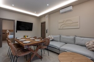 Una sala de estar moderna con una mesa de comedor, sofás y un televisor de pantalla plana montado en la pared.